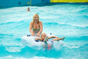 a woman with a child in a rubber inflatable circle plays in the pool of a summer water park in the rain photo