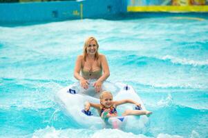 a woman with a child in a rubber inflatable circle plays in the pool of a summer water park in the rain photo