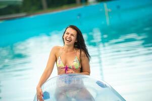 a woman in a bikini with a rubber inflatable circle playing and having a good time in the amusement park pool in the summer photo
