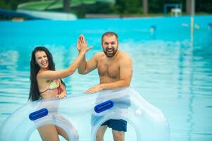 a man and a woman in a rubber inflatable circle stand against the background of the summer pool of the water park and clap their hands photo