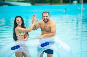a man and a woman in a rubber inflatable circle stand against the background of the summer pool of the water park and clap their hands photo