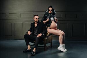 a pregnant woman in black clothes and a headscarf and a man in a suit in a studio on a dark background photo