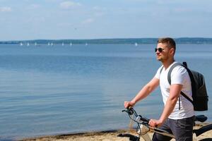 A cyclist with a backpack and glasses rides along the sea on a bicycle on a beautiful sunny day photo
