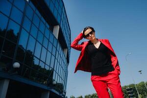 A girl in a red suit stands against the background of a modern building in the city photo