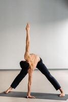 A man with a bare torso trains standing up, doing stretching in the gym photo