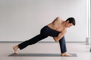 A man with a bare torso trains standing up, doing stretching in the gym photo