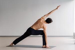 A man with a bare torso trains standing up, doing stretching in the gym photo