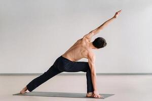 A man with a bare torso trains standing up, doing stretching in the gym photo