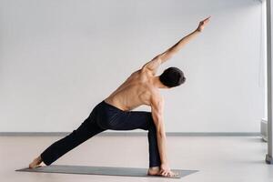 A man with a bare torso trains standing up, doing stretching in the gym photo