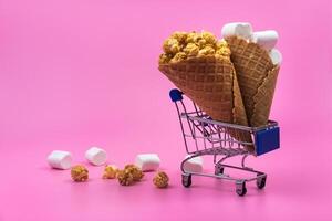 Shopping cart with ice cream cones with sweets on a pink background photo