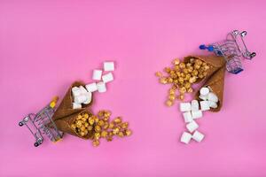 two shopping baskets with ice cream cones with sweets on a pink background photo
