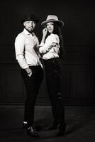 A man and a woman in white shirts and hats on a black background.A couple in love poses in the interior of the studio. black and white photo