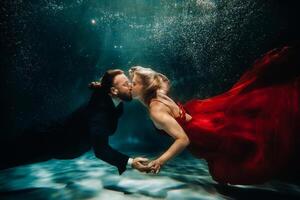 A woman in a red dress and a man in a suit are kissing underwater.A pair of floats under water photo