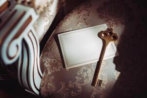 a postcard and an old key on the background of an old natural chair. Empty space for a postcard with your text. The view from the top of an old key and a blank card photo