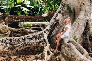 Summer portrait of a happy little girl on the island of Mauritius sitting on a huge tree.A girl sits on a large tree in the Botanical garden of the island of Mauritius photo