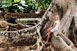 Summer portrait of a happy little girl on the island of Mauritius sitting on a huge tree.A girl sits on a large tree in the Botanical garden of the island of Mauritius photo