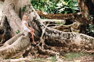 Summer portrait of a happy little girl on the island of Mauritius sitting on a huge tree.A girl sits on a large tree in the Botanical garden of the island of Mauritius photo