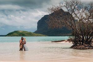 A girl in a swimsuit and a man in shorts stand in the ocean against the backdrop of mount Le Morne on the island of Mauritius.A couple in the water look into the distance of the ocean against photo