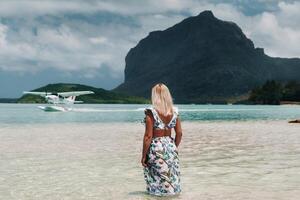 A girl in a swimsuit stands in the ocean and waits for a seaplane against the background of mount Le Morne on the island of Mauritius. photo