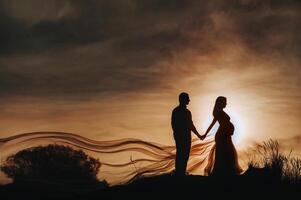 A loving man stands next to a pregnant woman at sunset, in the sand dunes. An unrecognizable Portrait of a beautiful newlywed couple expecting a baby.Lithuania, Nida photo