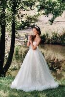 An elegant bride in a white dress, gloves with a bouquet on a waterfall in the Park, enjoying nature.Model in a wedding dress and gloves in the forest.Belarus photo
