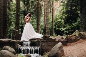 An elegant bride in a white dress and gloves holding a bouquet stands by a stream in the forest, enjoying nature.A model in a wedding dress and gloves in a nature Park.Belarus photo