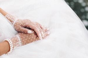 Close-up of the bride's hands in white transparent gloves near a waterfall in the Park.A model in a wedding dress and mesh gloves in a nature Park.Belarus photo