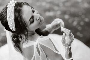 An elegant bride in a white dress, gloves and bare feet is sitting near a waterfall in the Park enjoying nature.A model in a wedding dress and gloves at a nature Park.Belarus. black and white photo