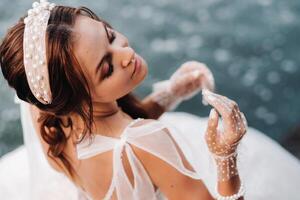 An elegant bride in a white dress, gloves and bare feet is sitting near a waterfall in the Park enjoying nature.A model in a wedding dress and gloves at a nature Park.Belarus. black and white photo