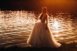 An elegant bride in a white dress enjoys nature at sunset.Model in a wedding dress in nature in the Park.Belarus photo