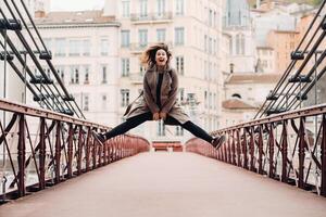 a girl in a coat with her hair down jumps emotionally on a bridge in the old city of Lyon. France. Girl in a coat in France photo