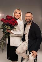 A man and a woman with flowers in their hands in strict clothes pose in the background in the studio photo
