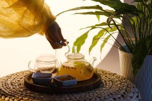 Close-up of a hand with a kettle. A teapot with sea buckthorn tea, honey and a plate with sea buckthorn on a tray photo