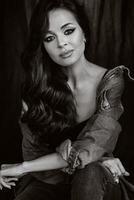 a brunette with long hair poses in the studio sitting on the floor on a black background.Black and white photo
