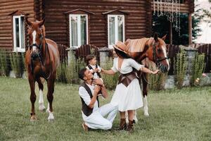 A family in white clothes with their son stand near two beautiful horses in nature. A stylish couple with a child are photographed with horses photo
