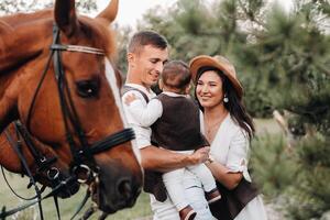 A family in white clothes with their son stand near two beautiful horses in nature. A stylish couple with a child are photographed with horses photo