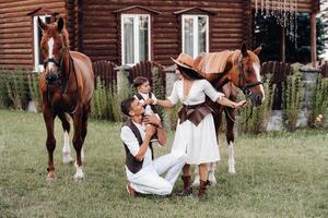 A family in white clothes with their son stand near two beautiful horses in nature. A stylish couple with a child are photographed with horses photo