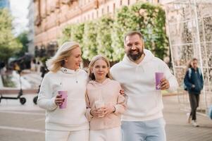 A happy family in white clothes walks in the city and drinks a drink photo