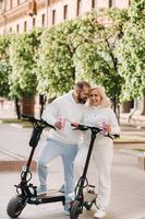 A couple in love in white clothes stands in the city on electric scooters with a drink in their hands photo