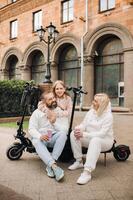 A family in white clothes stands in the city on electric scooters and drinks a drink photo