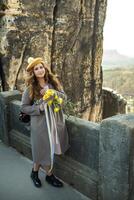 a girl in a gray coat and hat with a bouquet of flowers on the background of mountains and gorges in Swiss Saxony, Germany, Bastei photo