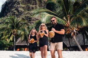 a stylish family in black clothes with coconuts in their hands on the beach of the island of Mauritius.Beautiful family on the island of Mauritius in the Indian ocean photo