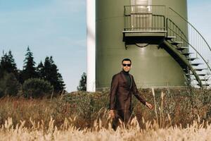 A man in a business suit with a green Golf shirt stands next to a windmill against the background of the field and the blue sky.Businessman near the windmills.Modern concept of the future. photo