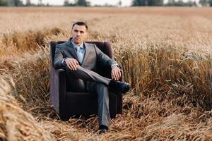 Portrait of a businessman in a gray suit and tie sitting in a chair in a wheat field photo