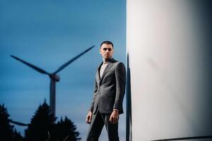 A man in a grey business suit stands next to a windmill after sunset .Businessman near windmills at night.Modern concept of the future. photo