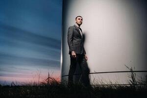 A man in a grey business suit stands next to a windmill after sunset .Businessman near windmills at night.Modern concept of the future. photo
