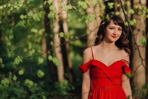 Spring Portrait of a laughing girl in a long red dress with long hair walking in the Park in the woods photo