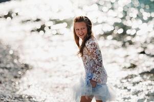 A little girl in a smart white dress walks along the embankment of lake Garda.A girl is photographed against the background of a mountain and lake in Italy.Torbole photo