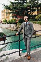 A man with a beard in a strict grey three-piece suit with a tie in the old town of Sirmione, a Stylish man in a grey suit in Italy photo