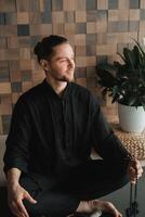 Portrait of a young man in a black kimano sitting in a lotus position on a gym mat in the interior photo